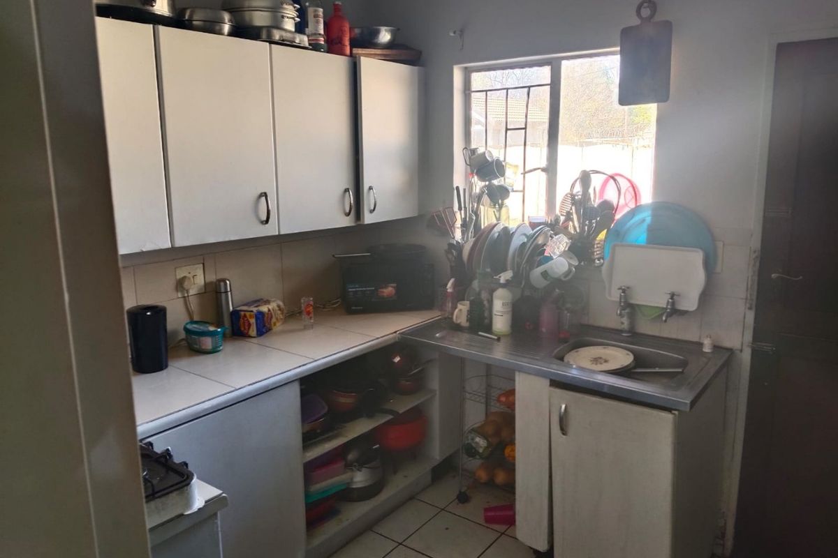 A compact kitchen featuring built-in cabinetry, a stainless steel sink, and tiled flooring, offering a functional layout with potential for modernization.