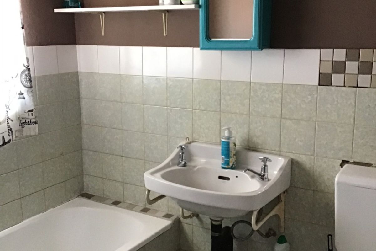 A functional bathroom featuring a wall-mounted basin, bathtub, and toilet with dated tiling and exposed plumbing fixtures.