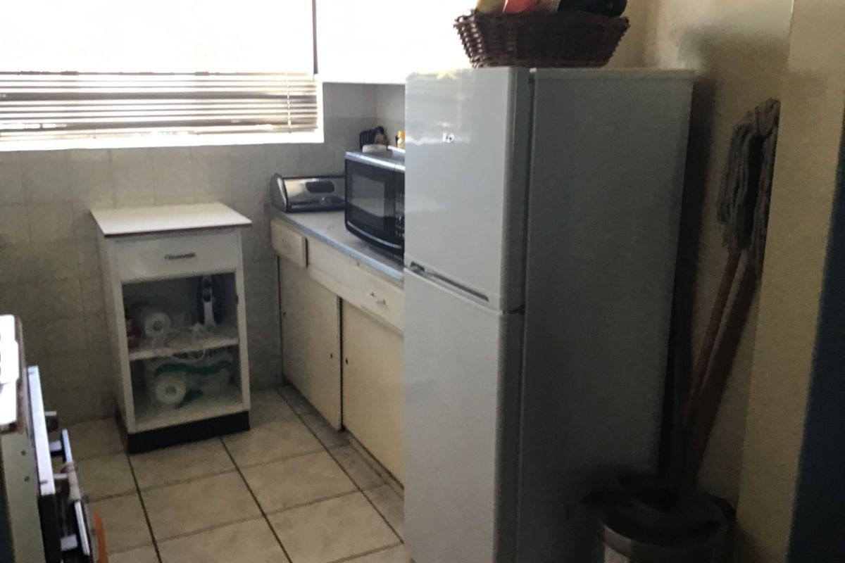 A compact kitchen featuring tiled flooring, tiled splashbacks, and dated built-in cabinetry with laminate countertops.