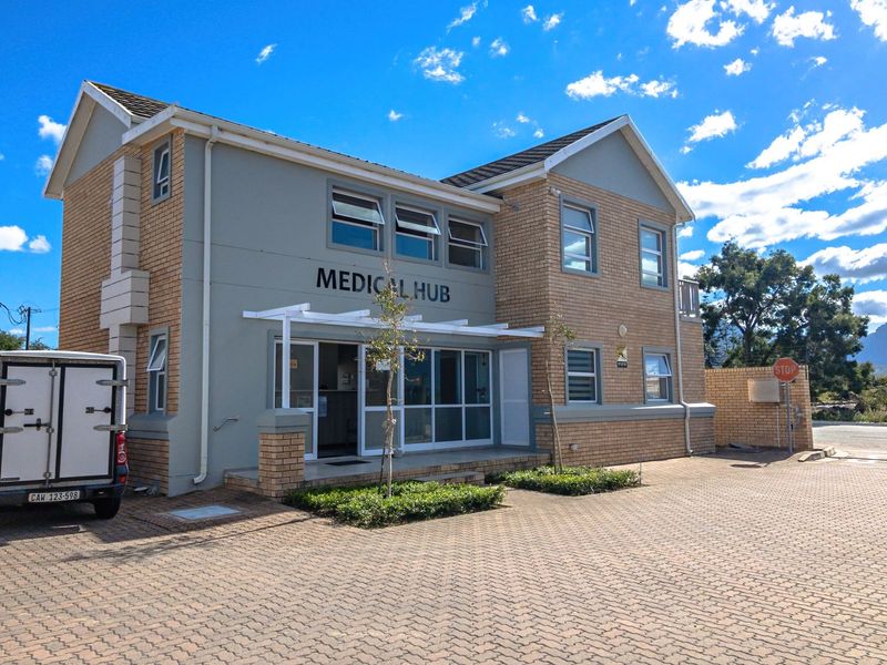 Front elevation of a two-story commercial medical facility featuring brick and plaster facade, paved parking area, and aluminium window frames.