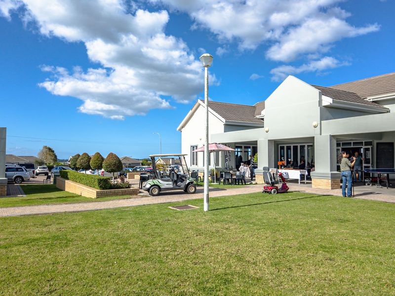 Exterior view of a modern clubhouse facility featuring a paved patio area, landscaped lawn, and well-maintained building structure.