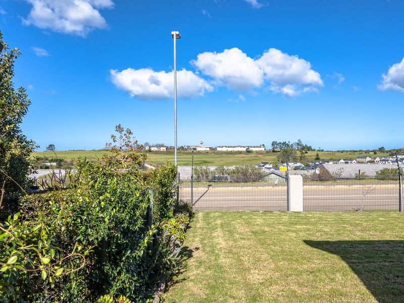 A clear, elevated view overlooking a residential neighborhood and open green space, featuring well-maintained lawn and secure perimeter fencing.