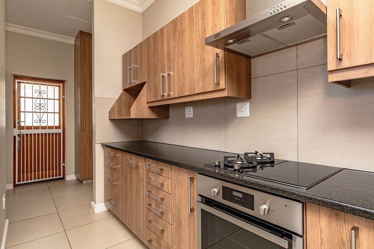 Modern kitchen featuring wood-look cabinetry, granite countertops, built-in oven, gas hob, and stainless steel extractor fan, with tiled flooring and a secure rear entrance.