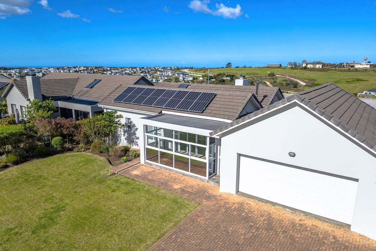Aerial view of a well-maintained residential property featuring a tiled roof with solar panels, a paved driveway, and an attached garage.