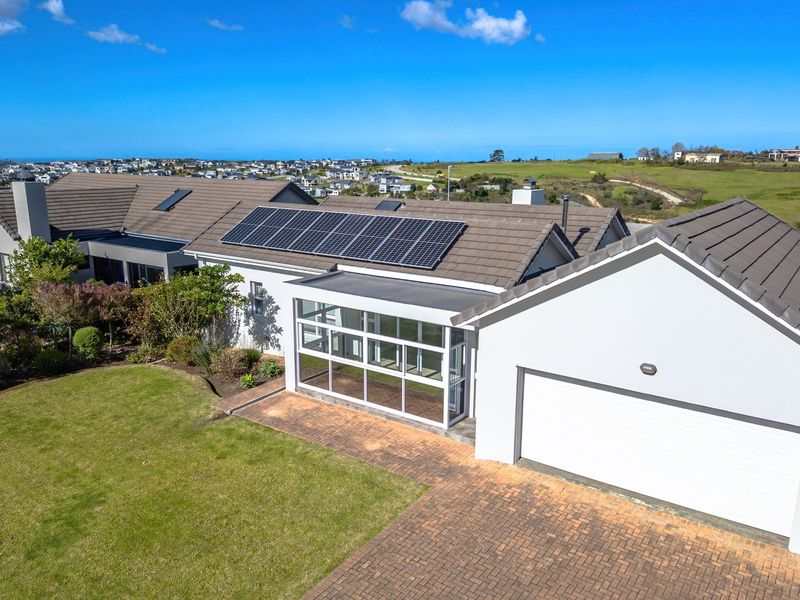 Aerial view of a well-maintained residential property featuring a tiled roof with solar panels, a paved driveway, and an attached garage.