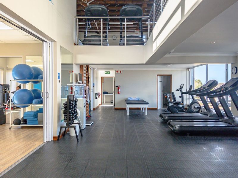 Spacious multi-level gym facility featuring durable rubber flooring, large windows for natural light, and a mezzanine level with stainless steel balustrades.
