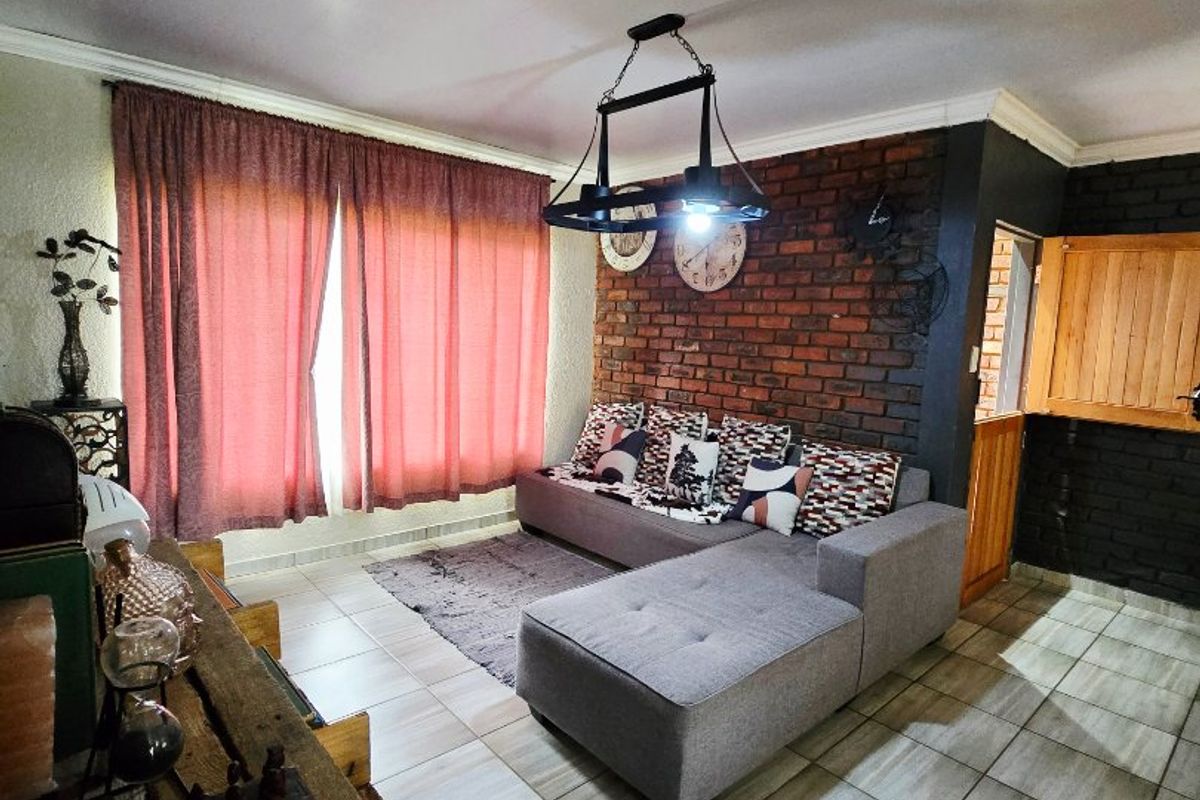A living room featuring an exposed brick accent wall, tiled flooring, and a central ceiling light fixture.