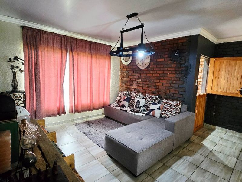 A living room featuring an exposed brick accent wall, tiled flooring, and a central ceiling light fixture.