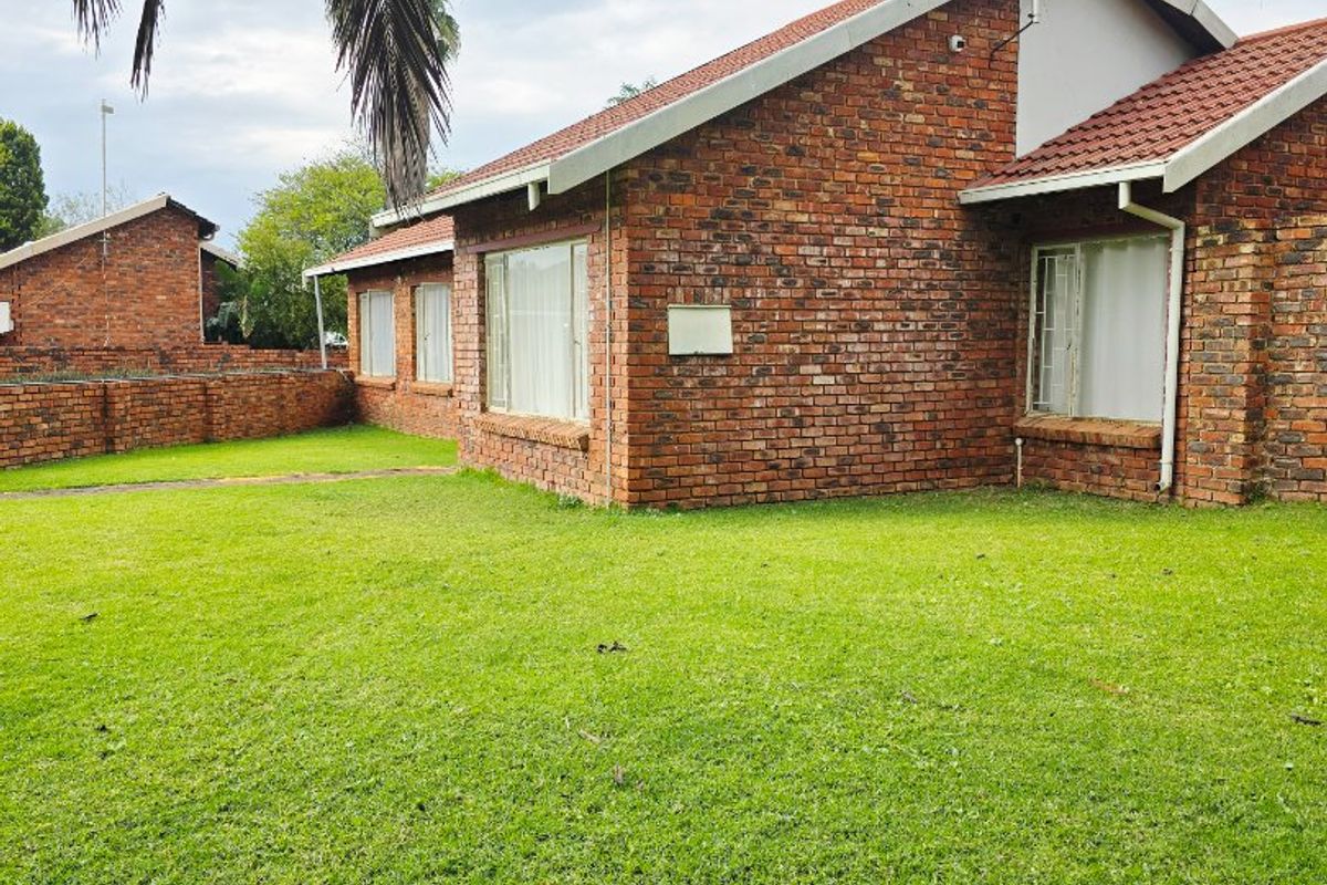 A view of the rear exterior of a face brick house featuring a tiled roof and a well-maintained lawn.
