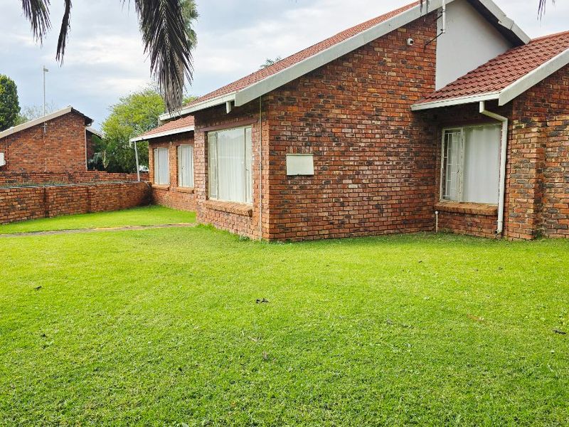 A view of the rear exterior of a face brick house featuring a tiled roof and a well-maintained lawn.