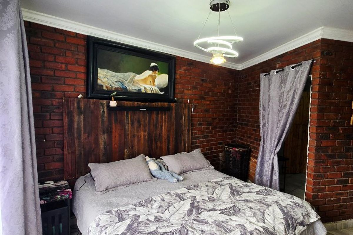 A cozy bedroom featuring exposed brick walls, tiled flooring, and a modern pendant light fixture with a custom wooden headboard.
