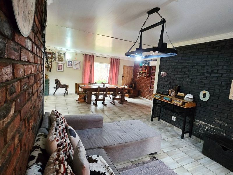 Spacious open-plan living and dining area featuring exposed and painted brick walls, tiled flooring, and modern pendant lighting.