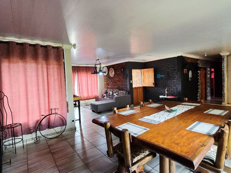 Spacious open-plan living and dining area featuring ceramic floor tiles and an exposed brick feature wall.