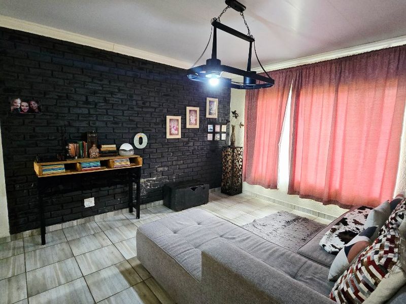A cozy living room featuring a striking black exposed brick feature wall, neutral tiled flooring, and a modern industrial-style pendant light fixture.