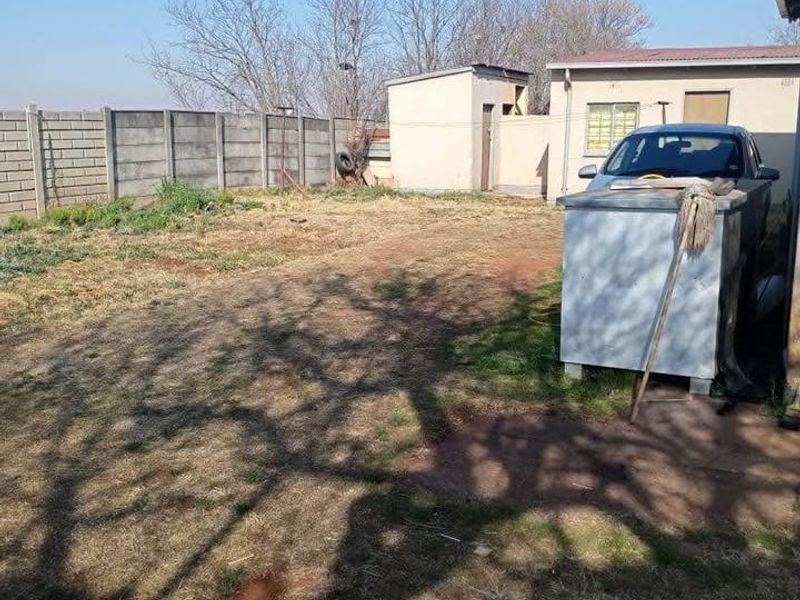 A rear exterior view of the property featuring a large yard, precast concrete boundary wall, and a detached outbuilding structure.