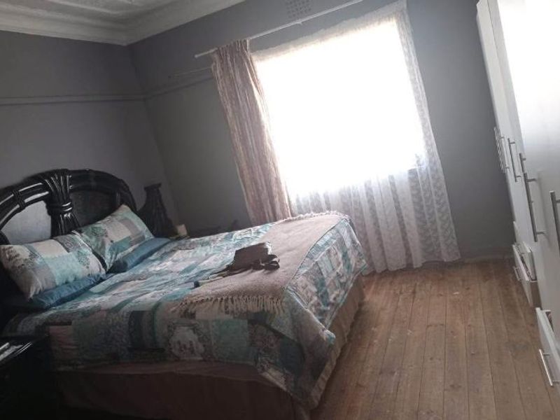 A bedroom featuring timber flooring, decorative ceiling cornices, and a built-in wardrobe, offering a functional space with potential for cosmetic updates.