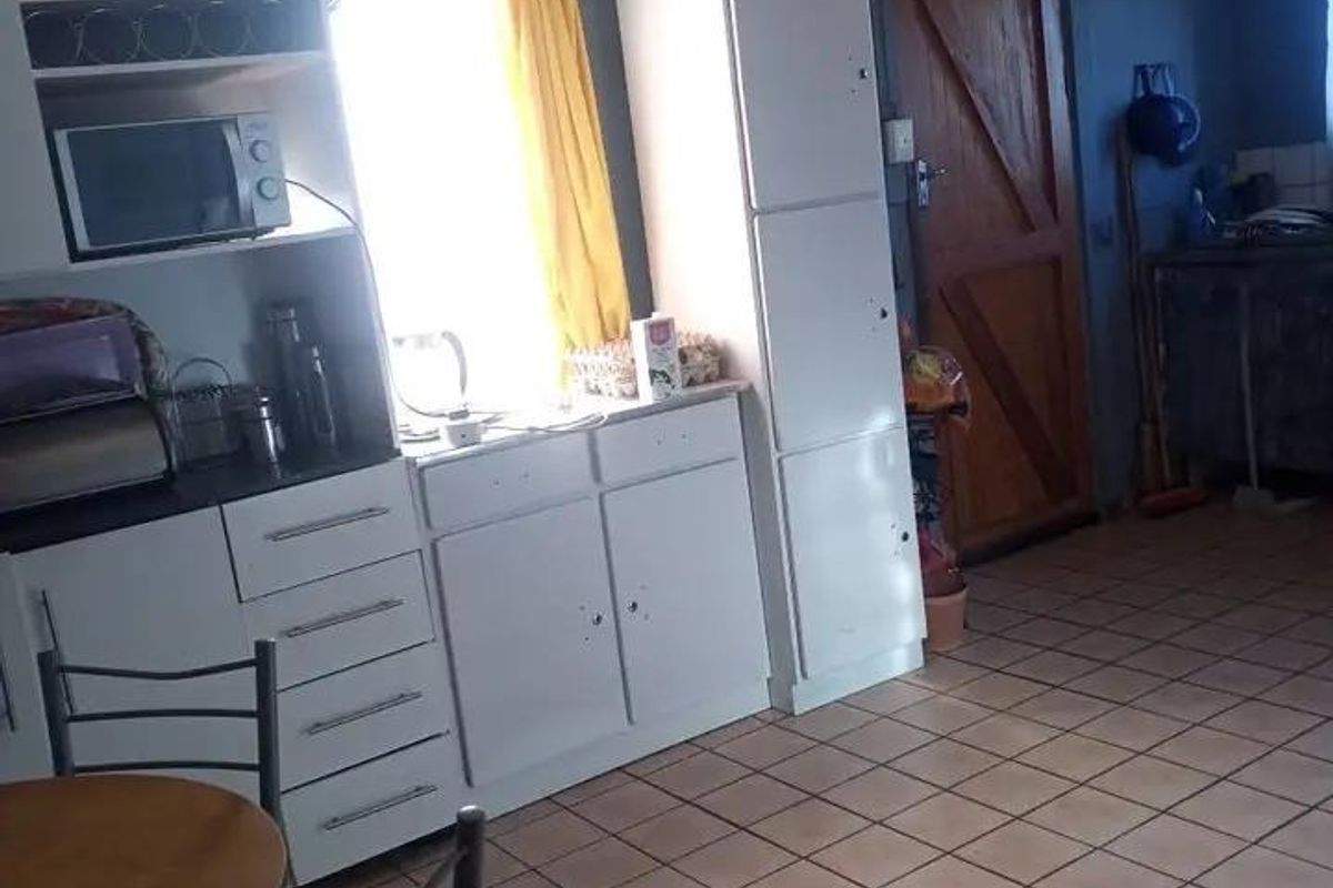 A dated kitchen area featuring white built-in cabinetry, tiled flooring, and a timber door, requiring cosmetic updates to improve its overall condition.