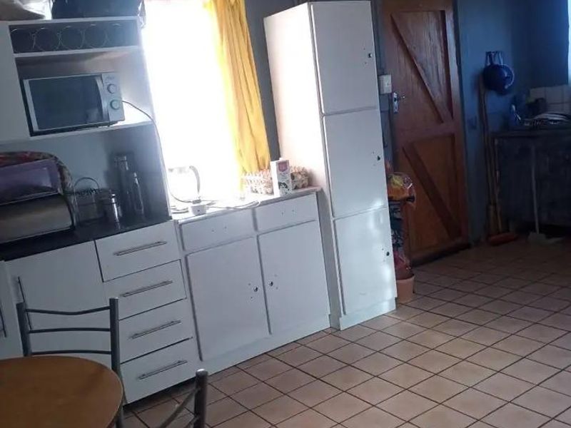 A dated kitchen area featuring white built-in cabinetry, tiled flooring, and a timber door, requiring cosmetic updates to improve its overall condition.