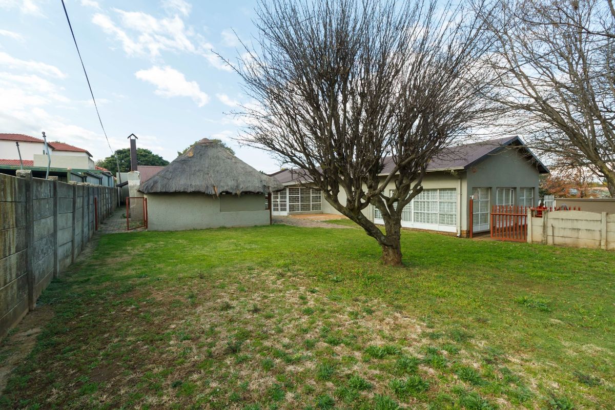 Spacious rear garden featuring a traditional thatched lapa, established lawn, and secure precast concrete boundary walls.
