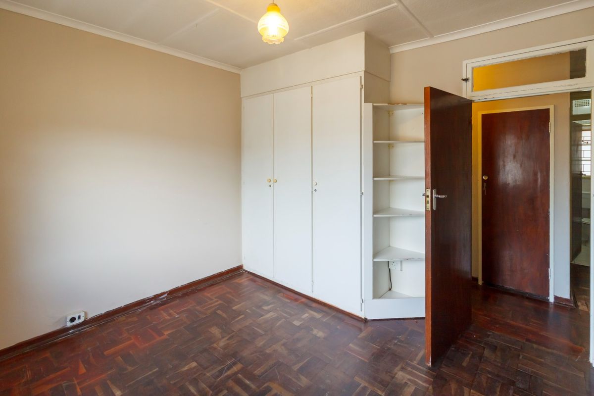 A vacant bedroom featuring original parquet flooring, built-in storage cupboards with open shelving, and a traditional timber door.