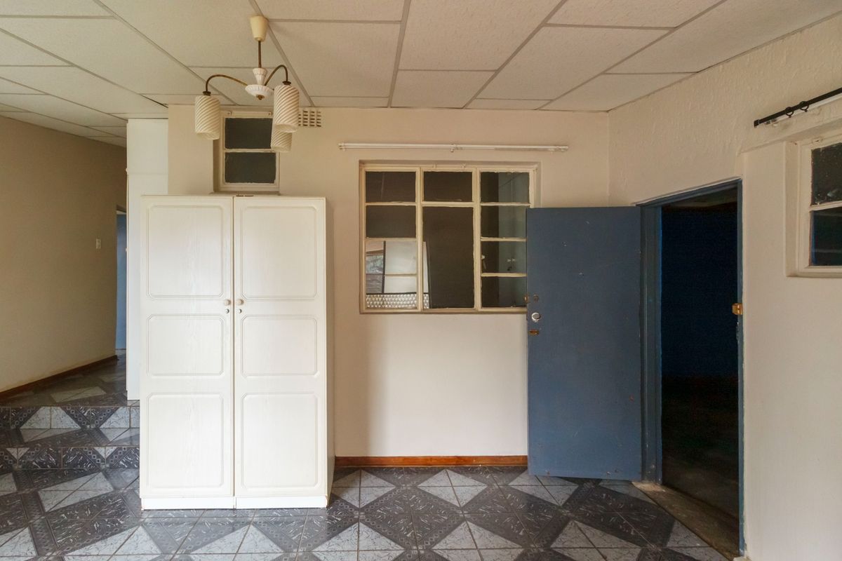 A dated living area featuring tiled flooring, a drop ceiling, and an internal window, offering a blank canvas for renovation and modernization.