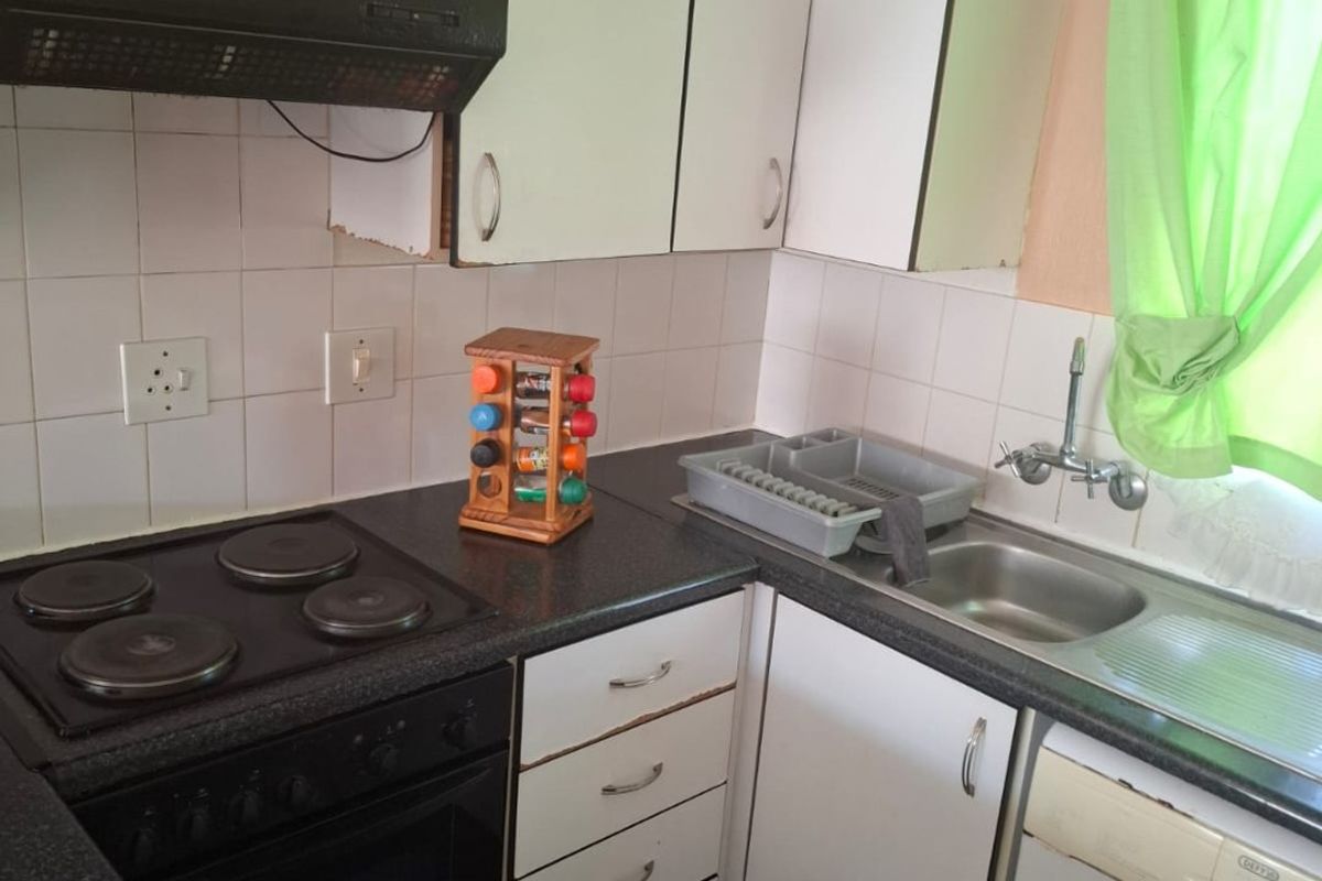 Compact kitchen featuring built-in cabinetry, electric hob, oven, extractor fan, and stainless steel sink with tiled backsplash.