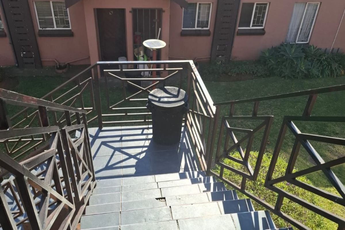 Exterior view of an apartment building featuring a tiled staircase with metal balustrades leading down to a communal garden area.