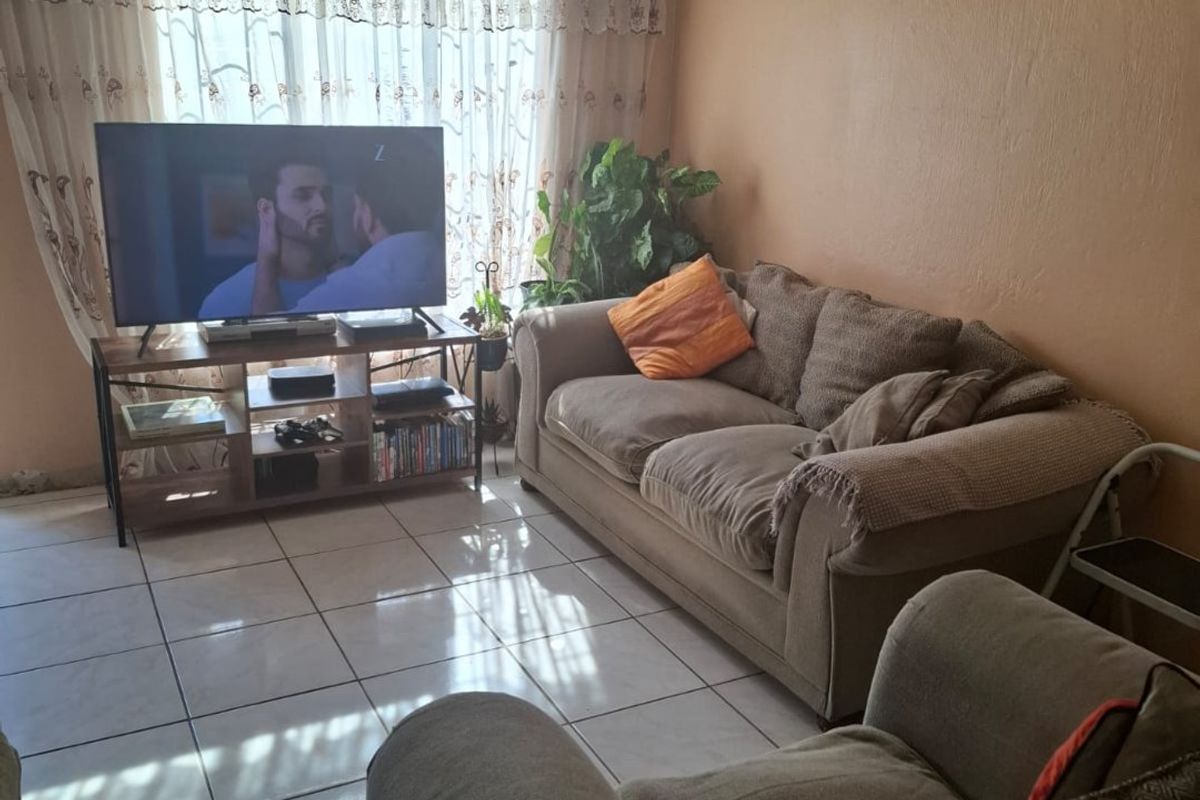 A living room featuring tiled flooring and natural light through a large window with curtain rails.
