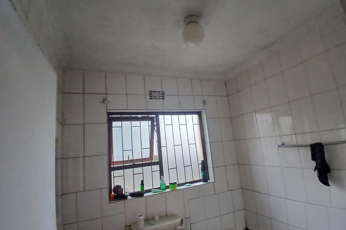 A basic bathroom featuring full-height wall tiling, a window with security bars, and a towel rail, currently in need of cosmetic updates.
