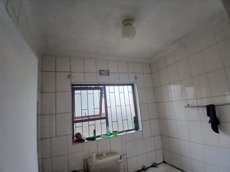A basic bathroom featuring full-height wall tiling, a window with security bars, and a towel rail, currently in need of cosmetic updates.