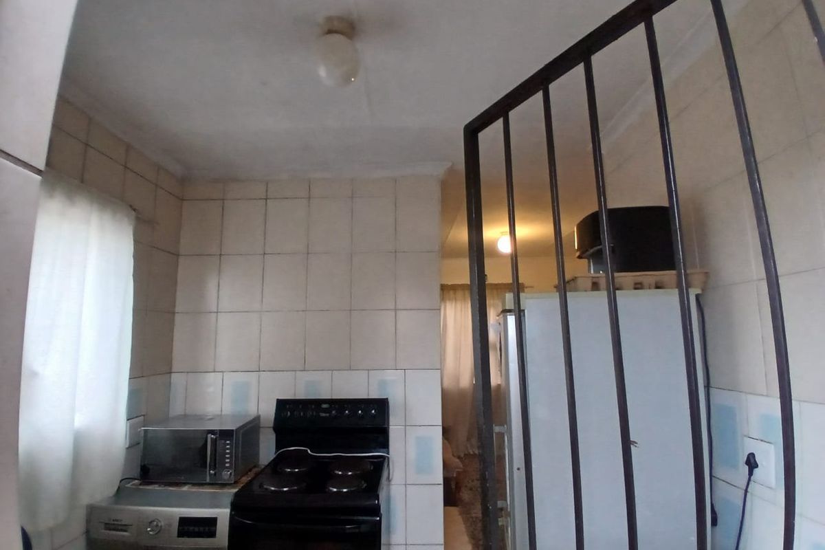 A compact kitchen area featuring tiled walls, a built-in stove, and a security gate, requiring cosmetic updates to improve its overall condition and appeal.
