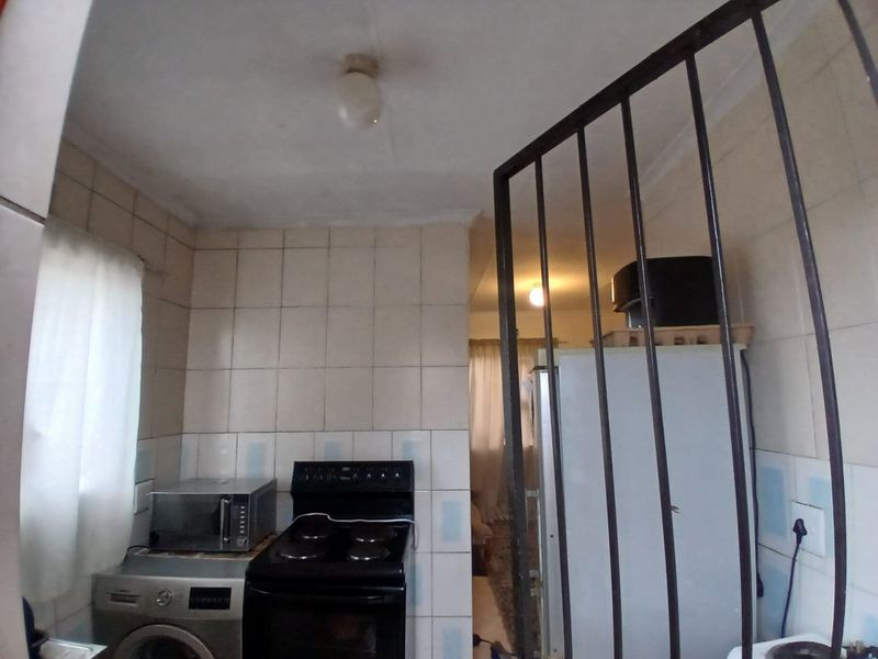 A compact kitchen area featuring tiled walls, a built-in stove, and a security gate, requiring cosmetic updates to improve its overall condition and appeal.