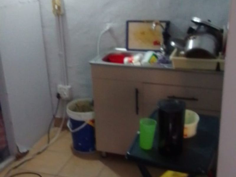 A small utility or laundry area featuring a basic sink unit, tiled flooring, and exposed electrical wiring.
