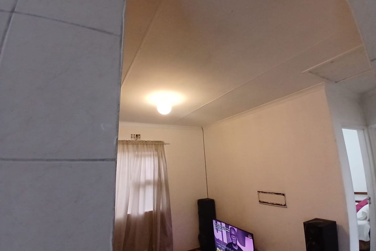 A living room area featuring standard ceiling cornicing and a central light fixture, with a visible wall mounting point.