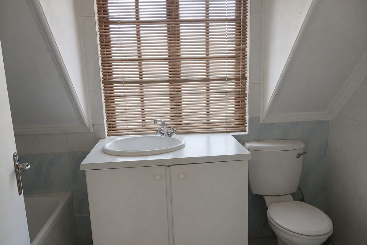 A functional bathroom featuring a vanity with basin, toilet, and bathtub, set under a sloped ceiling with natural light.