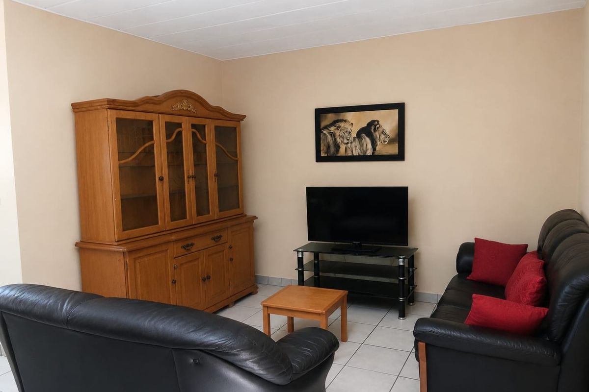 A living room featuring neutral wall tones, tiled flooring, and a panelled ceiling, providing a functional and comfortable space for relaxation.