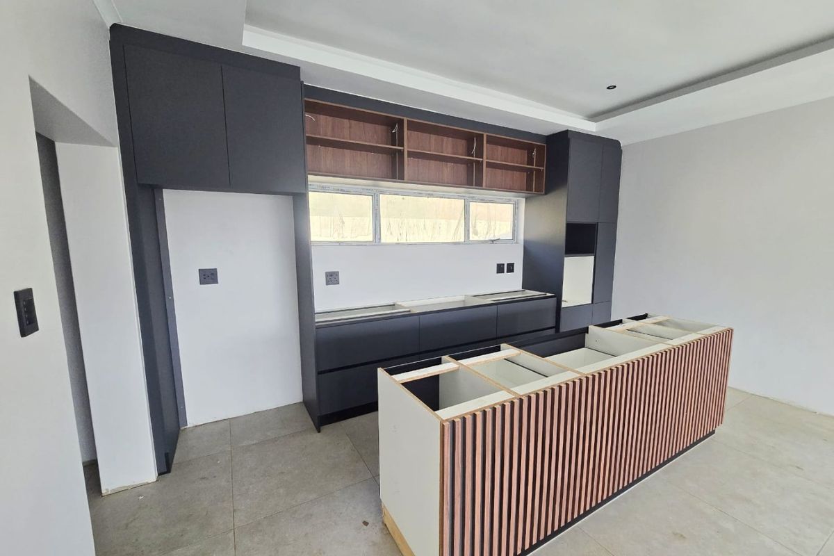 Modern kitchen featuring dark cabinetry, a central island with slatted wood detailing, and recessed lighting. The space is currently unfinished and awaiting final installation.