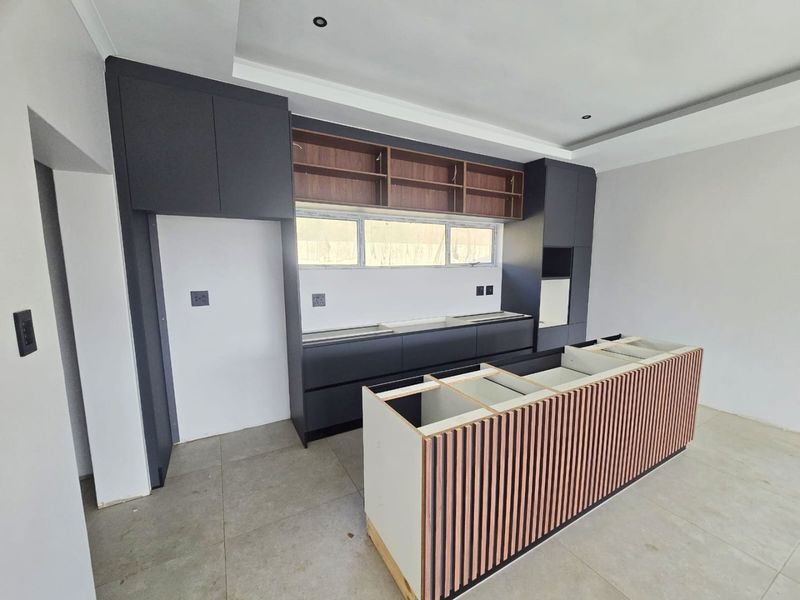 Modern kitchen featuring dark cabinetry, a central island with slatted wood detailing, and recessed lighting. The space is currently unfinished and awaiting final installation.