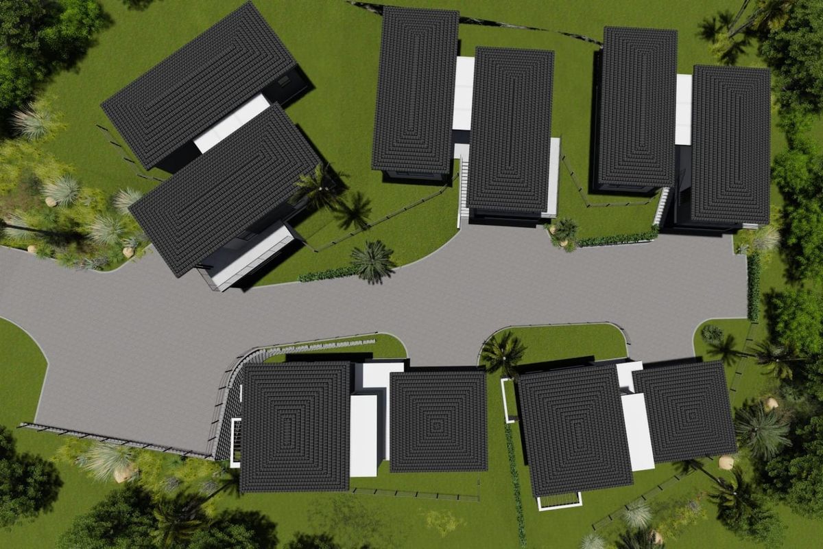 An aerial view of a residential development featuring multiple detached houses with dark tiled roofs, connected by a paved driveway and surrounded by landscaped grounds.