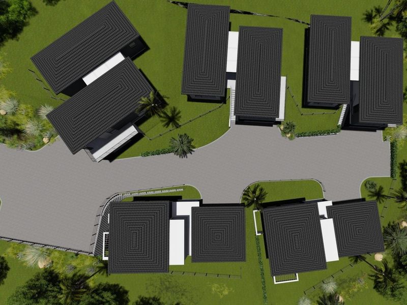 An aerial view of a residential development featuring multiple detached houses with dark tiled roofs, connected by a paved driveway and surrounded by landscaped grounds.