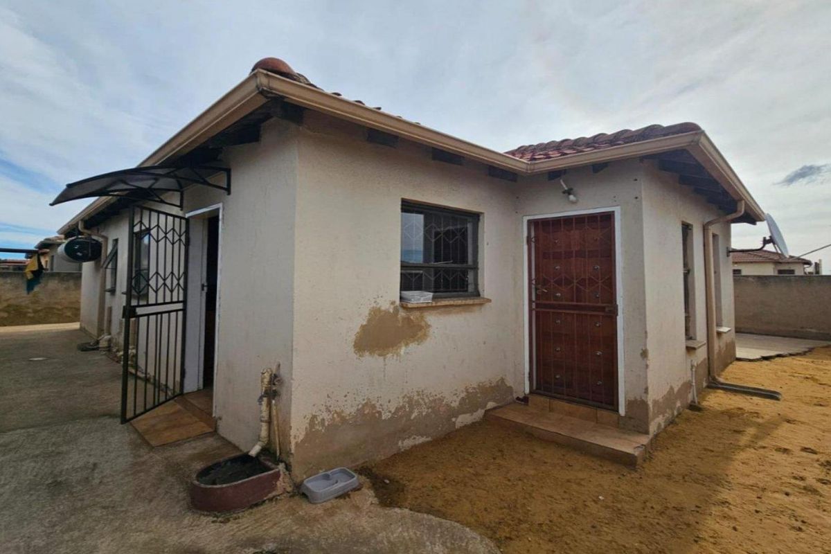 Rear exterior view of the house showing masonry walls with visible plaster damage, security gates, and tiled roofing.