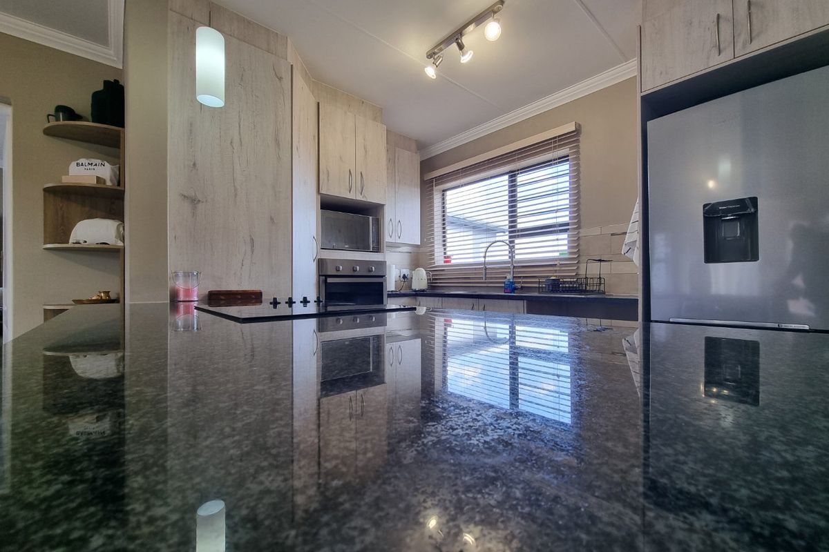 Modern kitchen featuring granite countertops, built-in oven, hob, and light wood-finish cabinetry with ample storage and a functional layout.