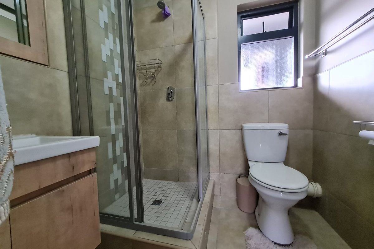 A functional bathroom featuring a glass-enclosed shower, a vanity unit with a basin, and a standard toilet, finished with neutral wall and floor tiles.