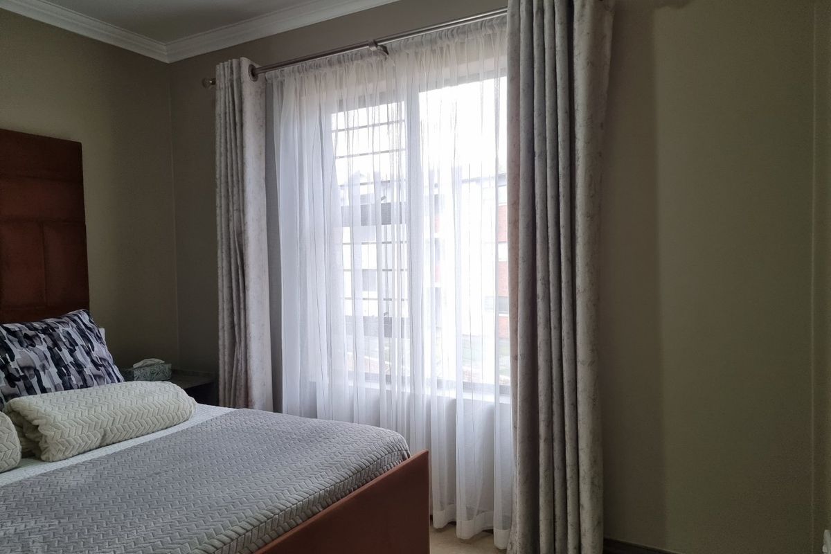 A well-maintained bedroom featuring tiled flooring, crown molding, and a window fitted with security bars.