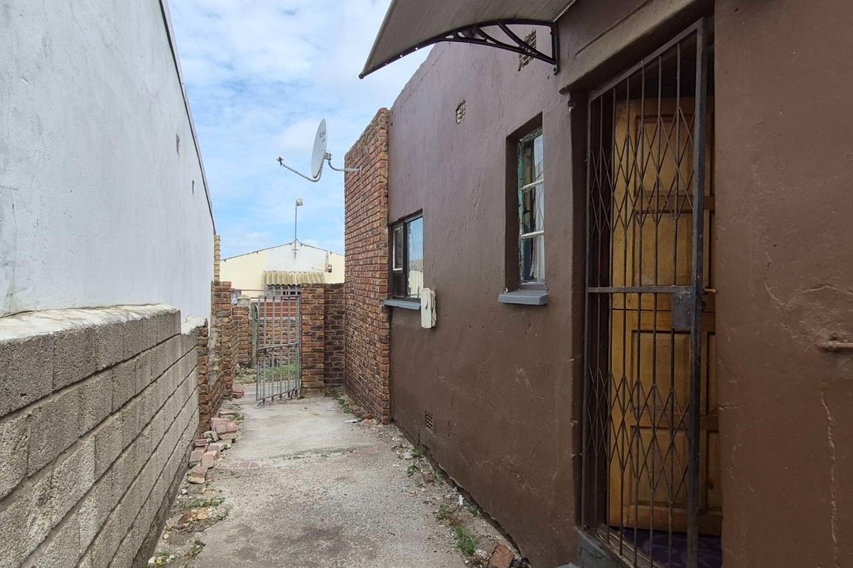 A narrow rear exterior passage featuring a concrete walkway, brick boundary walls, and a security gate entrance to the property.