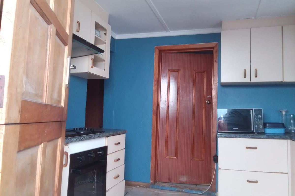 A compact kitchen featuring built-in cabinetry, a built-in oven with hob, and an extractor fan, finished with tiled flooring and blue wall paint.