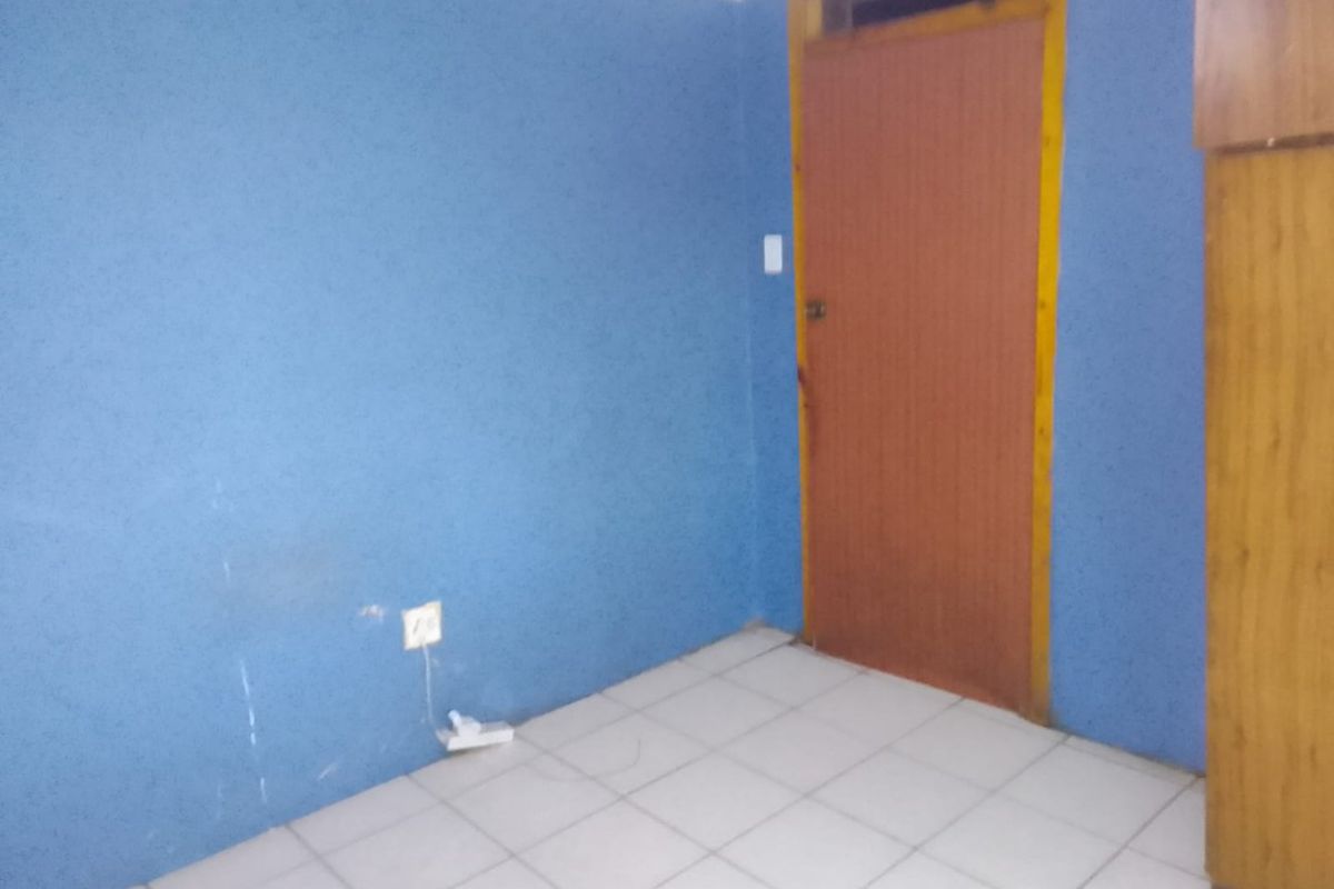 A simple, empty bedroom featuring tiled flooring and a timber door, providing a blank canvas for potential interior design updates.