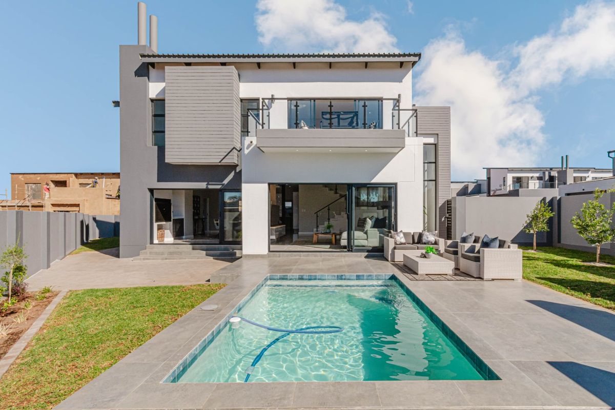 Modern double-story rear elevation featuring a swimming pool, tiled patio area, and an upper-level balcony with glass balustrades.