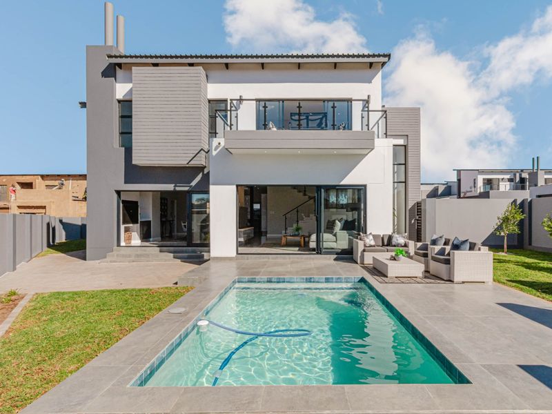 Modern double-story rear elevation featuring a swimming pool, tiled patio area, and an upper-level balcony with glass balustrades.