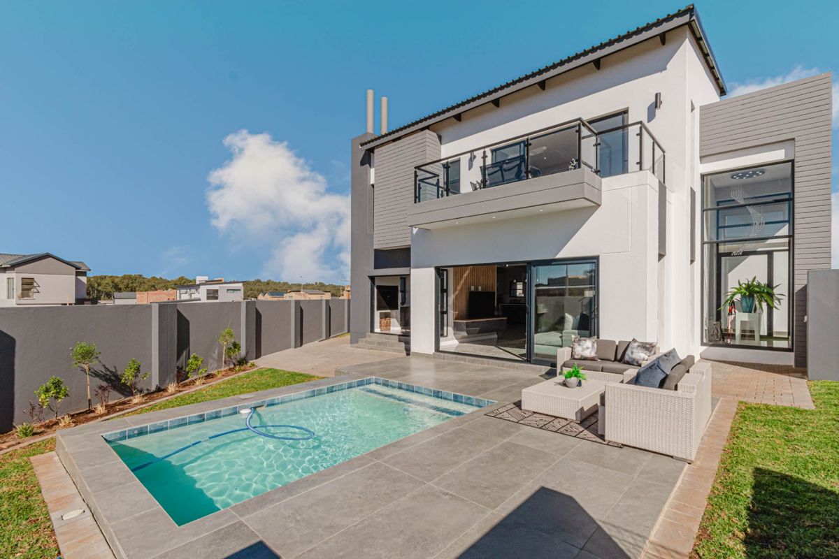 Modern double-storey rear elevation featuring a tiled patio, swimming pool, and an upper-level balcony with glass balustrades.